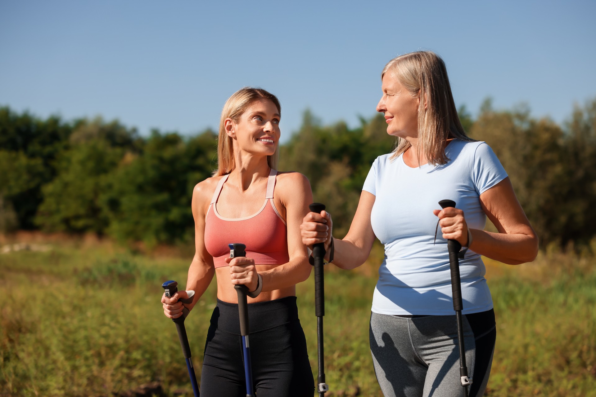 Happy women practicing Nordic walking with poles outdoors on sunny day